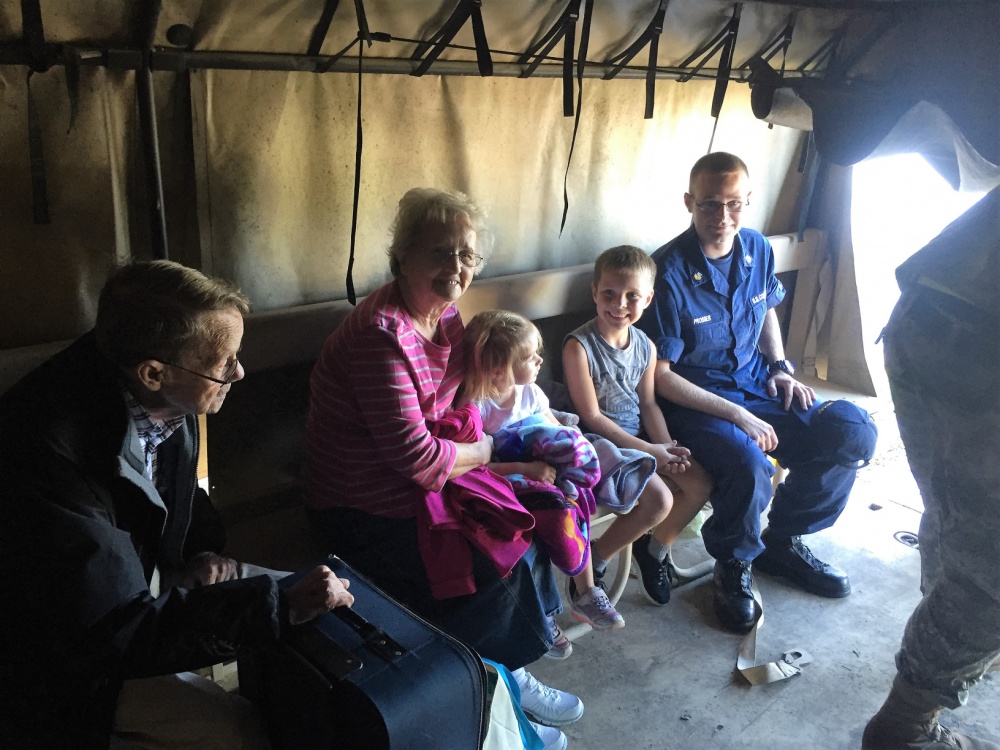 80-year-old Nancy Sykes, 82-year-old R.D. Sykes, six-year-old son Ethan Prosser, two-year-old Annalynne Prosser and Petty Officer 1st Class James Prosser take a moment to regroup on a North Carolina Air National Guard 236th Brigade Engineer Battalion M35 2-ton cargo truck in Lumberton, North Carolina, Oct. 10, 2016. The town experienced catastrophic flooding requiring evacuations for many residents. (U.S. Coast Guard photo by Master Chief Petty Officer Louis Coleman/Released)